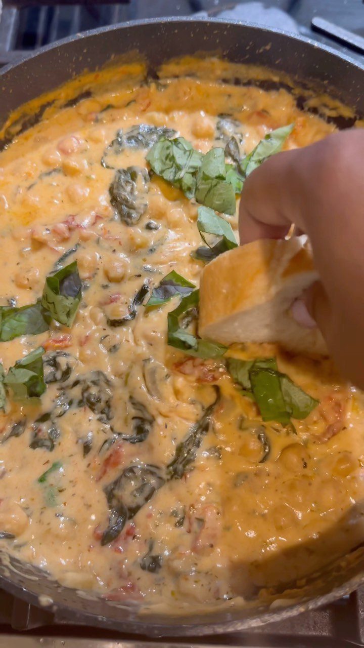 Creamy chickpea stew with spinach and basil in a skillet with bread dipping.