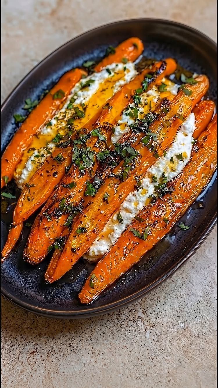 Roasted carrots on a bed of whipped cheese garnished with fresh green herbs.