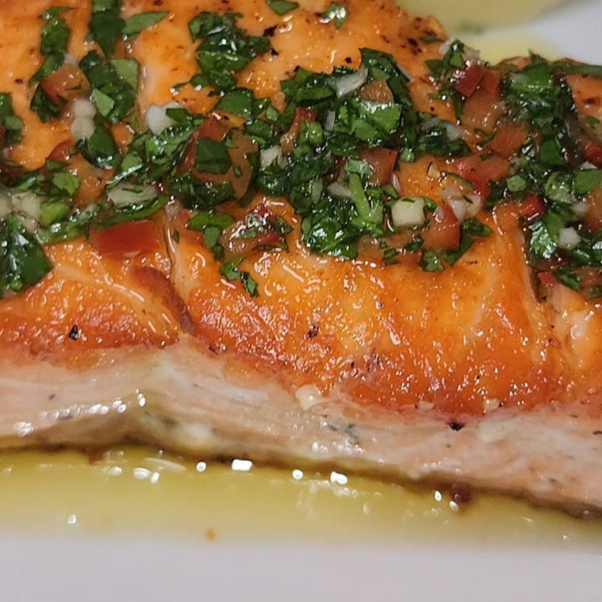 Cooked salmon fillet topped with fresh herb and tomato salsa on white plate