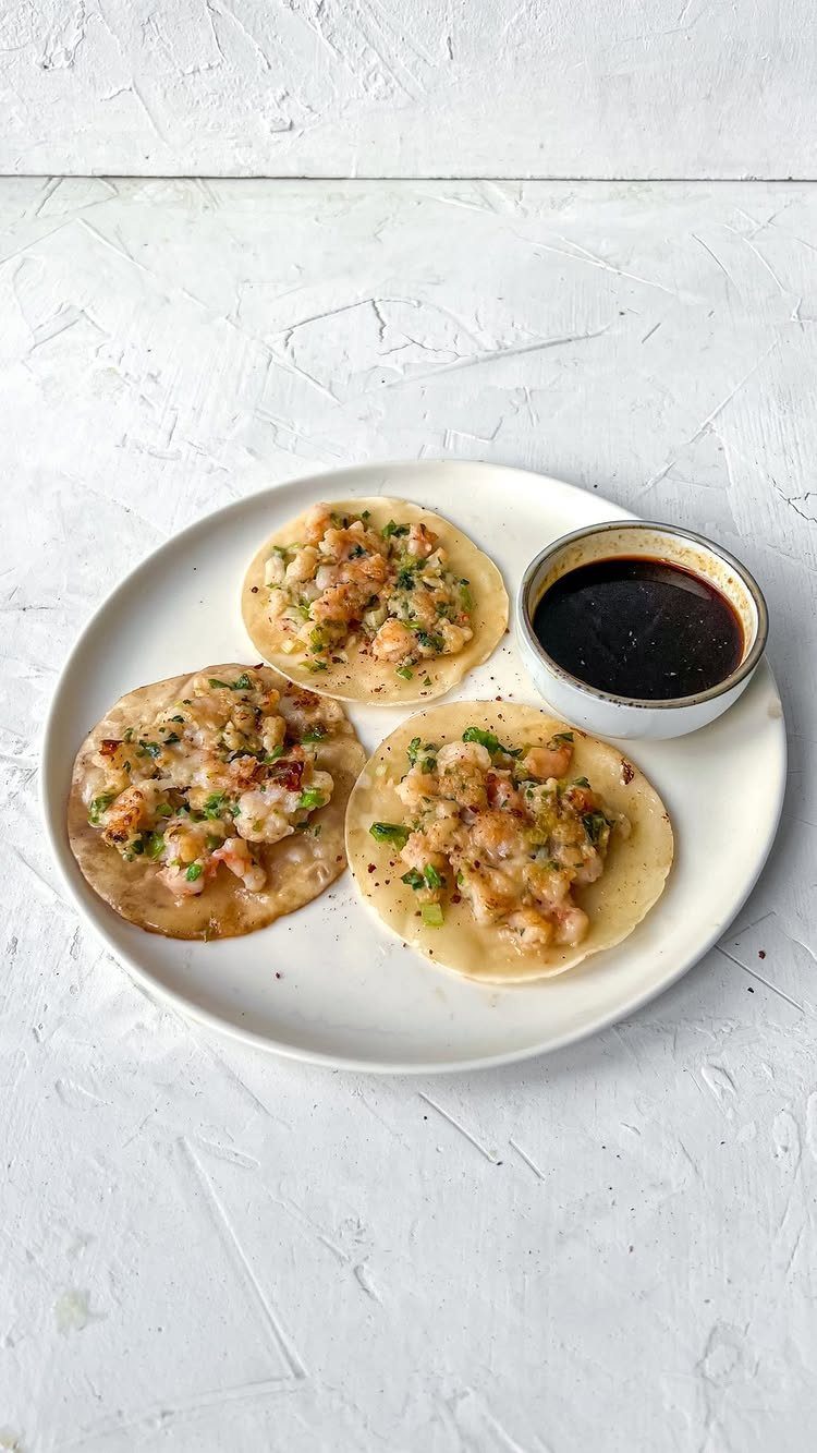 Three pan-fried smash dumplings with shrimp and green onions and a dipping sauce.