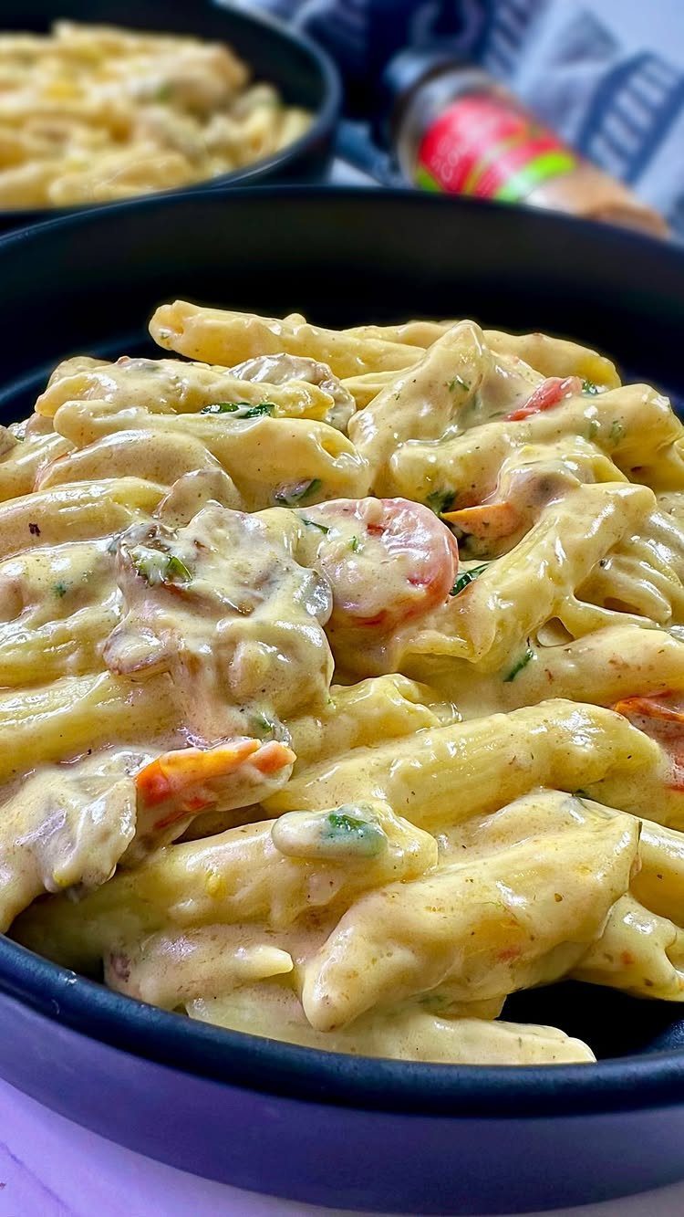 Penne pasta with creamy sauce, mushrooms, and spinach in a black bowl.