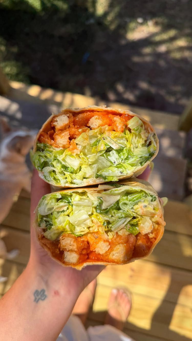 Two halves of a buffalo chicken wrap with lettuce and dressing held outdoors.