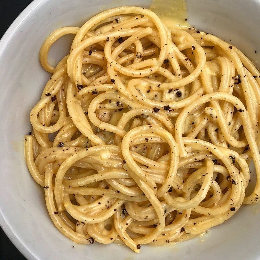 Spaghetti with creamy cheese sauce and black pepper in a white bowl.
