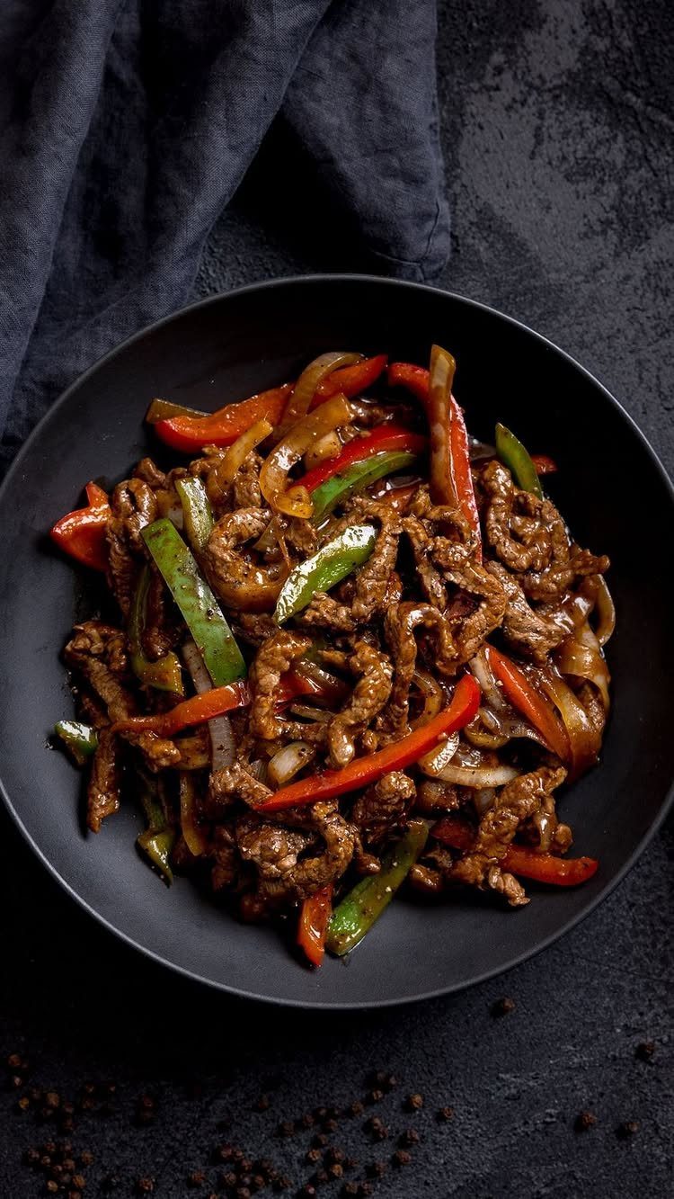 Beef stir fry with red and green peppers in a black bowl