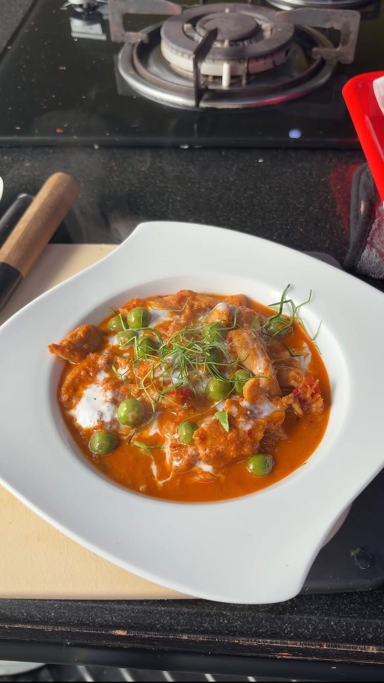 Orange-red chicken curry with green peas and cream in a white bowl.