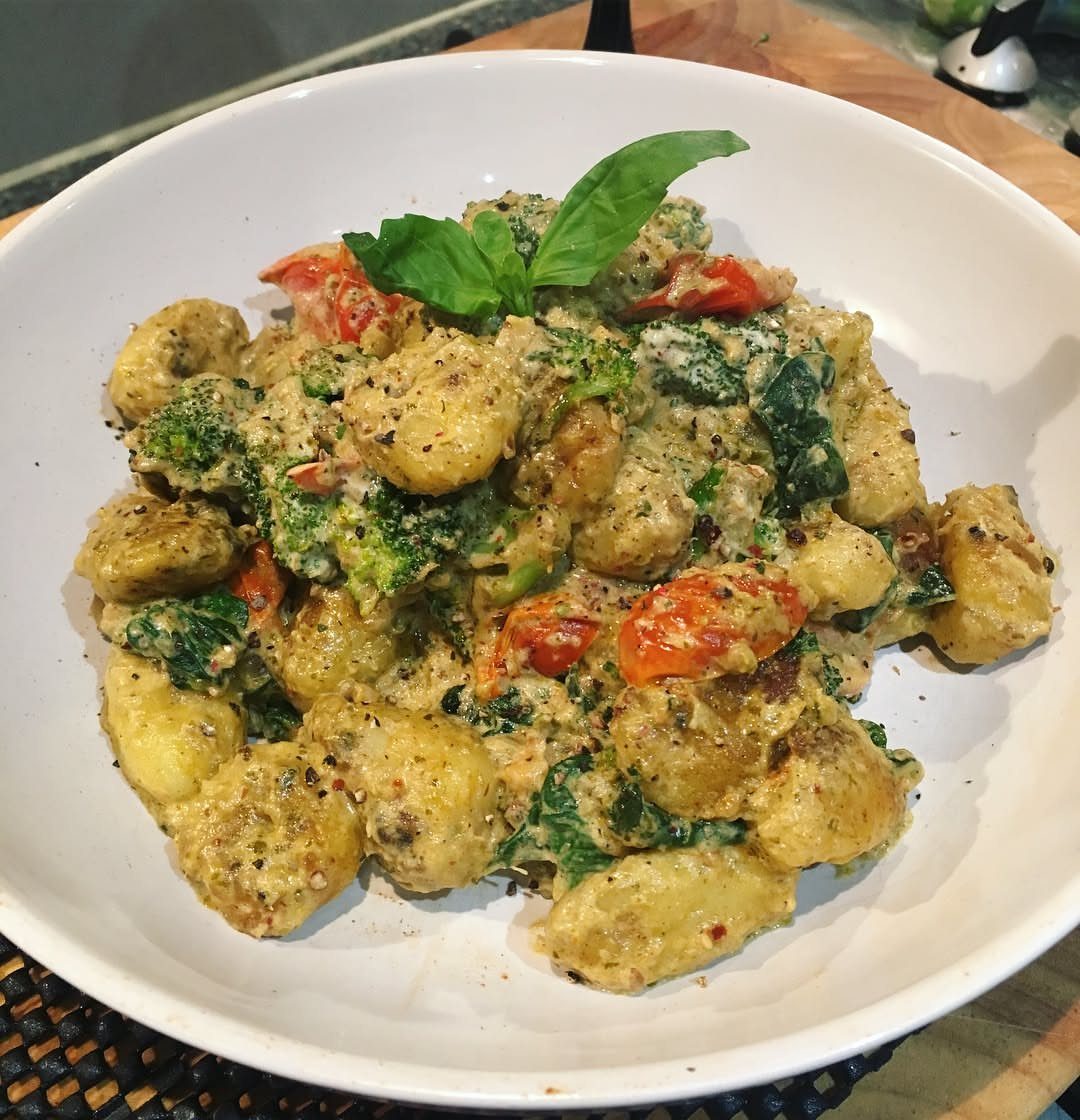 Creamy gnocchi with broccoli, cherry tomatoes, and spinach topped with a basil leaf.