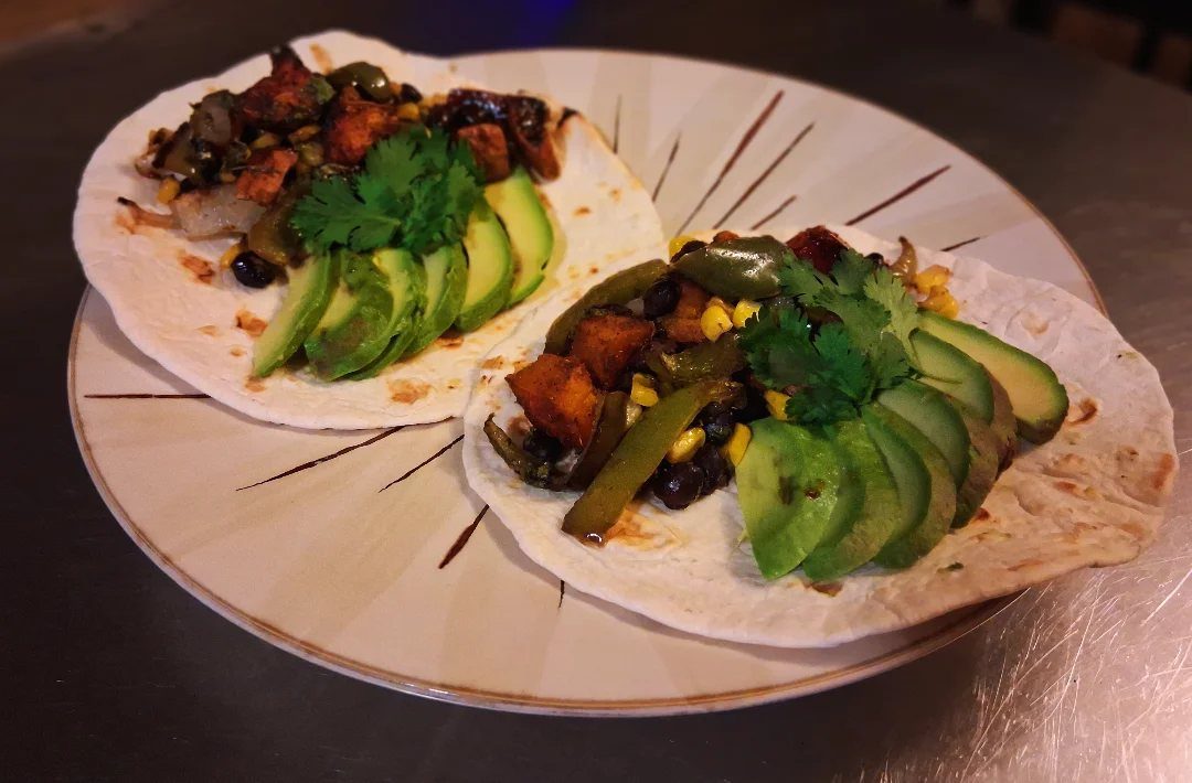 Two sweet potato and black bean tacos topped with avocado and cilantro.