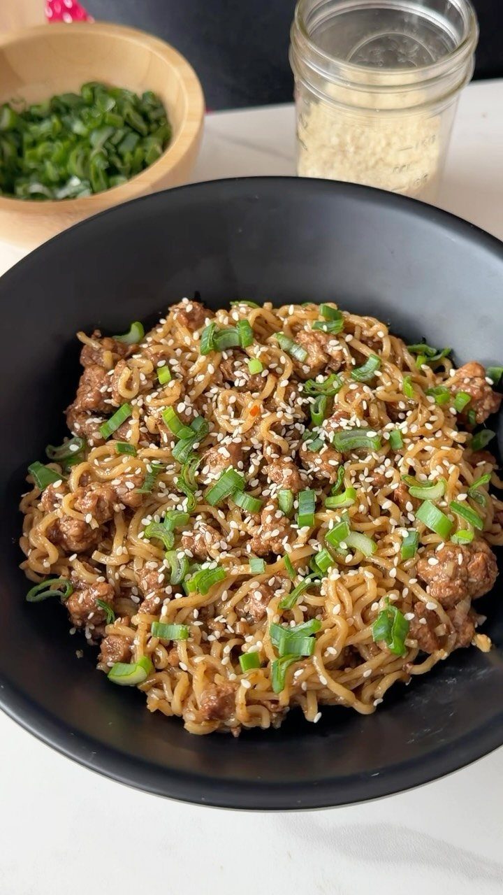 Noodles with ground meat, green onions, and sesame seeds in a black bowl.