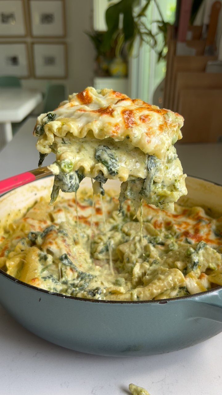Cheesy spinach lasagna slice lifted from a grey pot with melted cheese strings.
