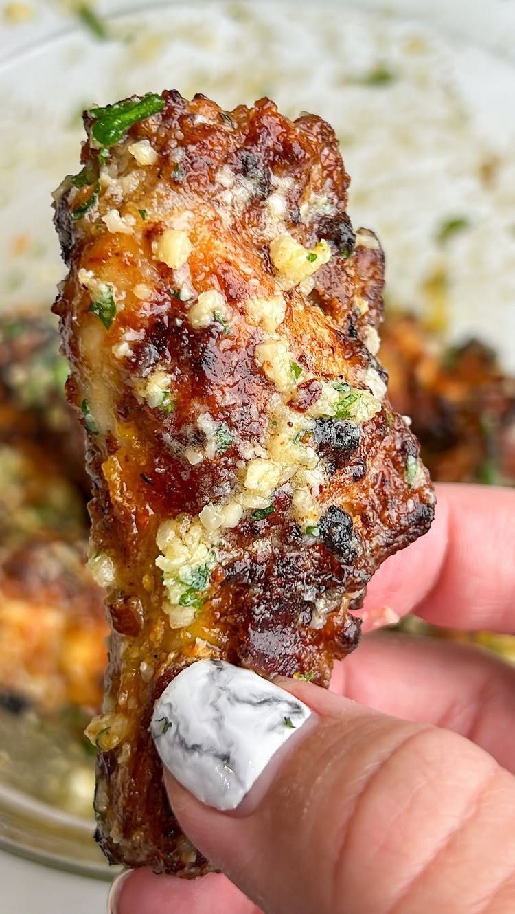 Garlic chicken wing with minced garlic and herbs held by a hand.