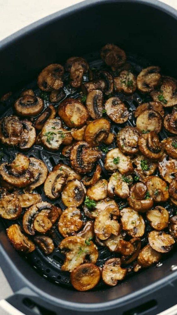Browned sliced mushrooms with herbs inside a black air fryer basket.