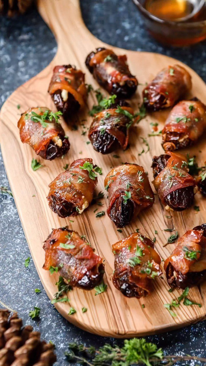 Bacon wrapped dates with parsley on a wooden board with honey in background