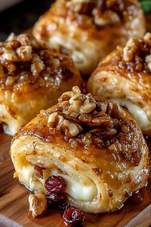 Baked brie bites in puff pastry topped with glazed walnuts and dried cranberries.