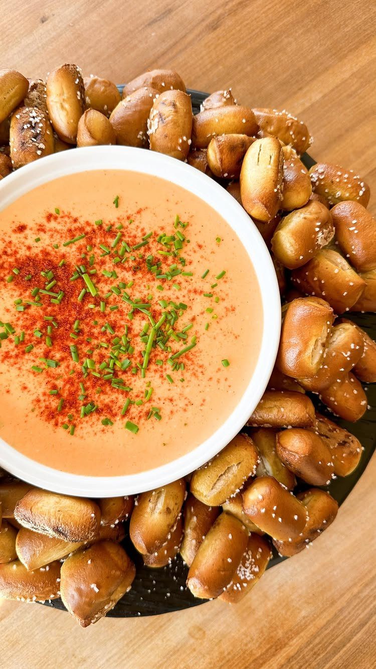 Orange creamy cheese dip with chives surrounded by salted pretzel bites on platter.