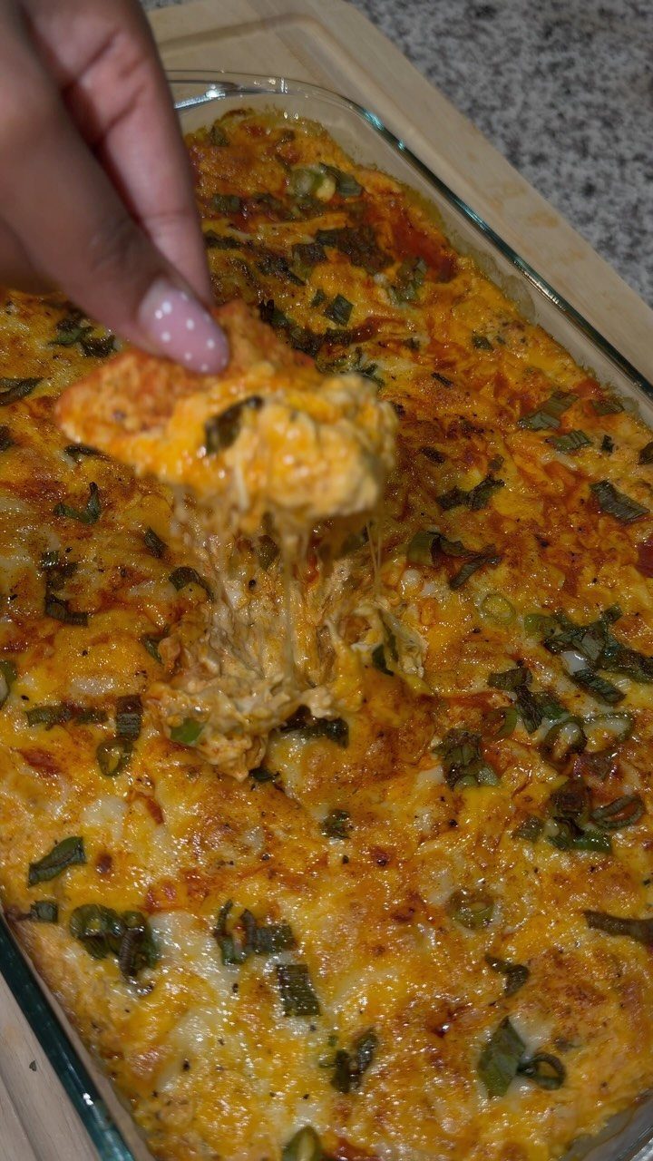 Cheesy buffalo chicken dip in a glass dish with a chip lifting melted cheese.