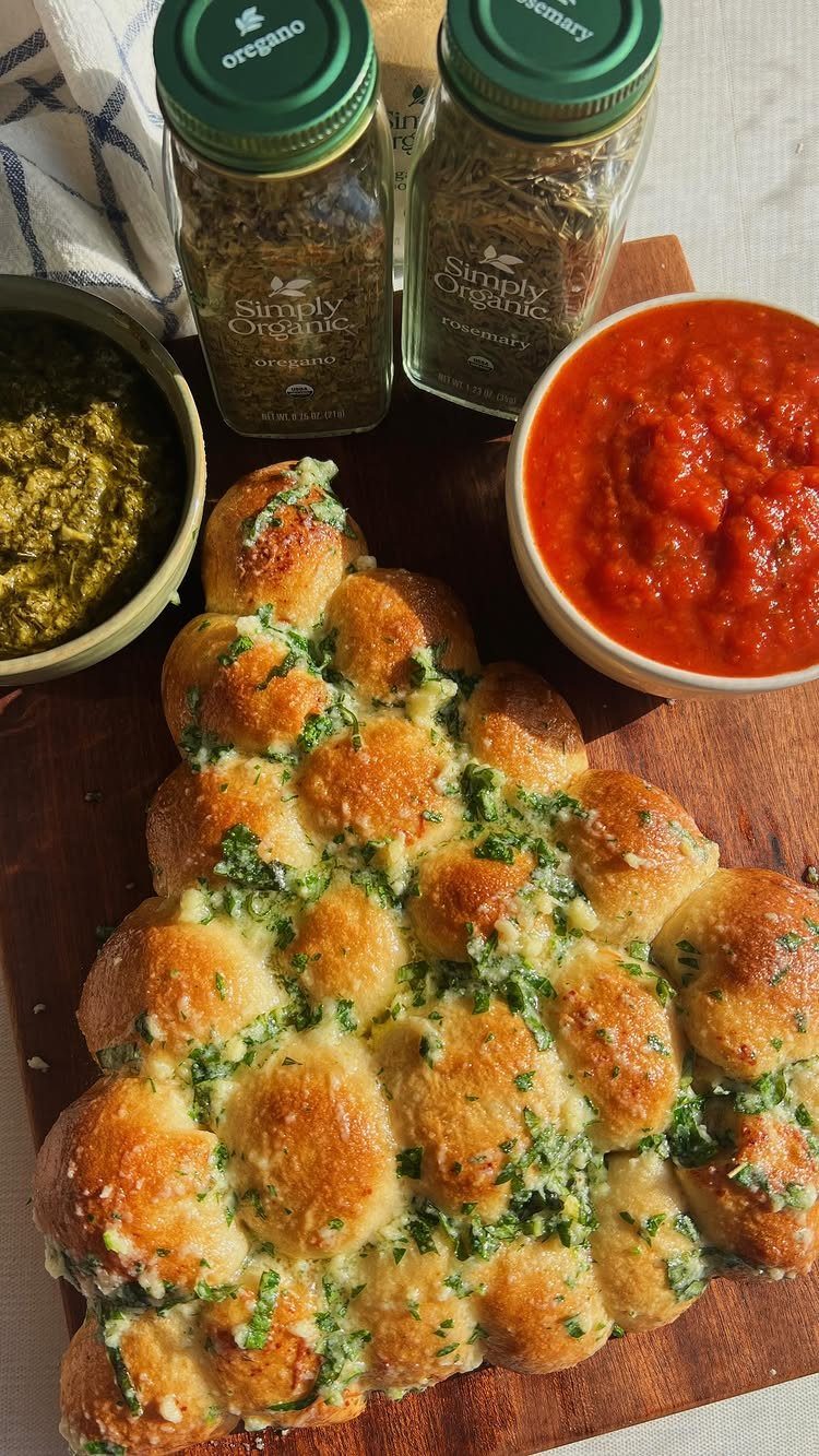 Cheesy garlic pull apart bread on a wooden board with marinara and pesto dips.