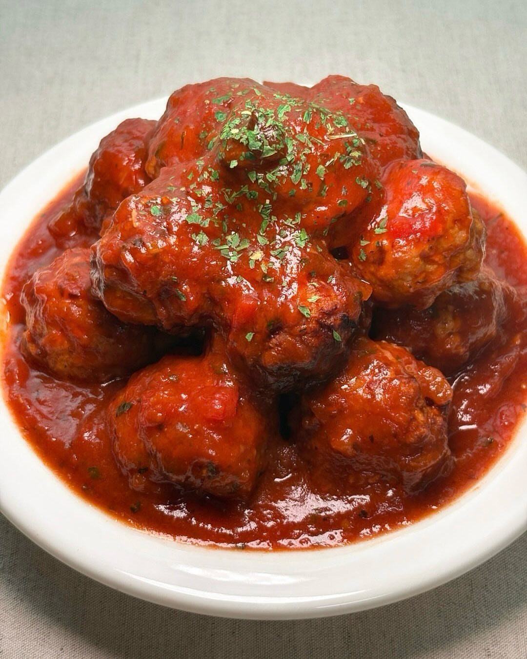 Meatballs in red sauce garnished with herbs in a white ceramic bowl.