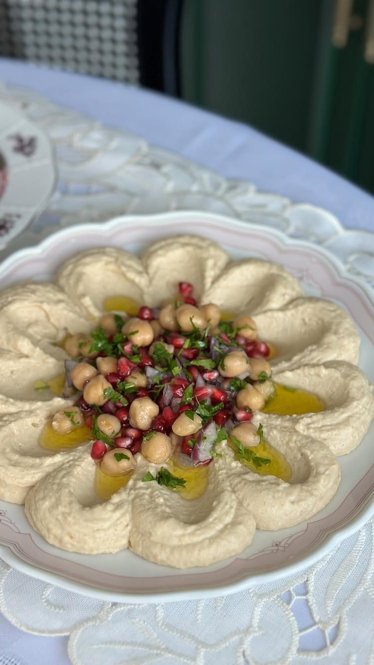 Creamy hummus topped with chickpeas, pomegranate seeds, and parsley on a white plate.
