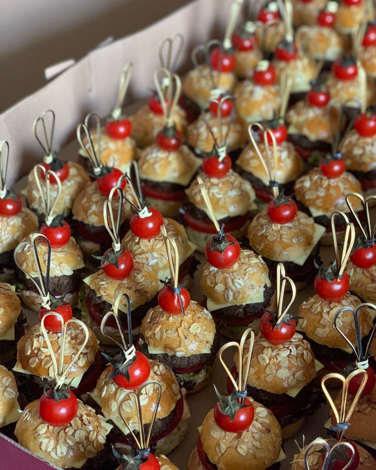 Mini beef sliders with cheese and cherry tomatoes on decorative bamboo skewers.