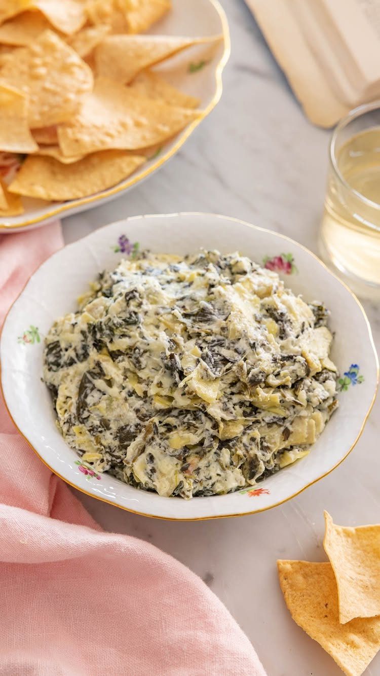 Creamy spinach artichoke dip in a floral bowl with tortilla chips and wine.