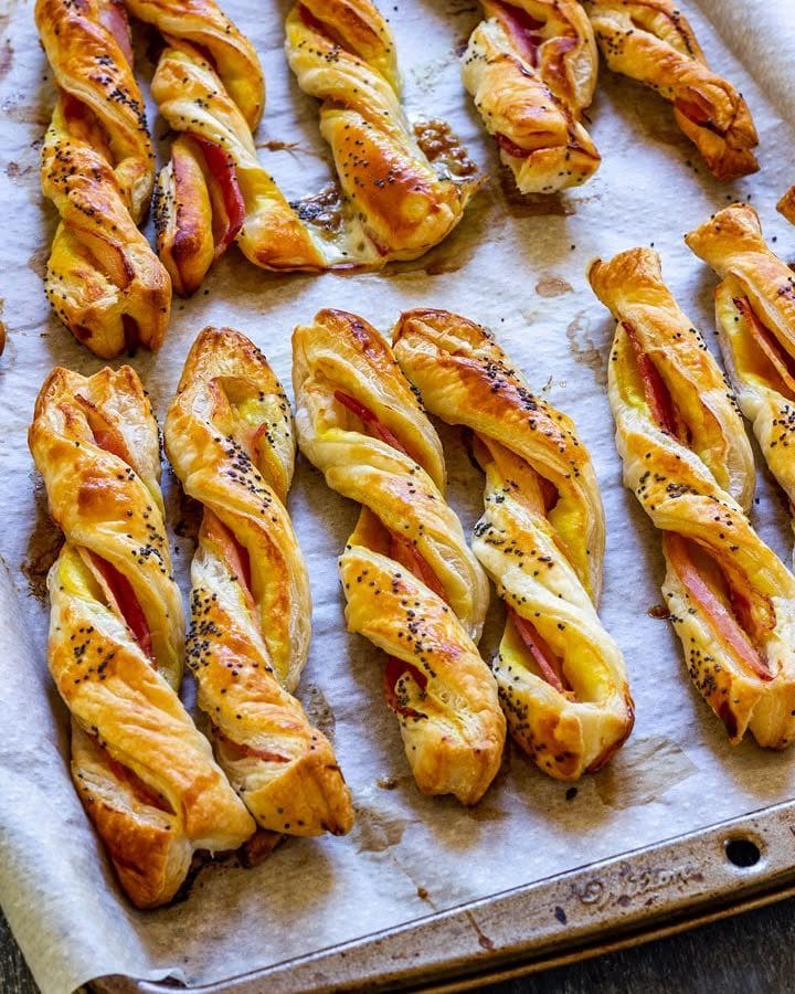 Twisted puff pastry strips with bacon and cheese on a baking sheet.