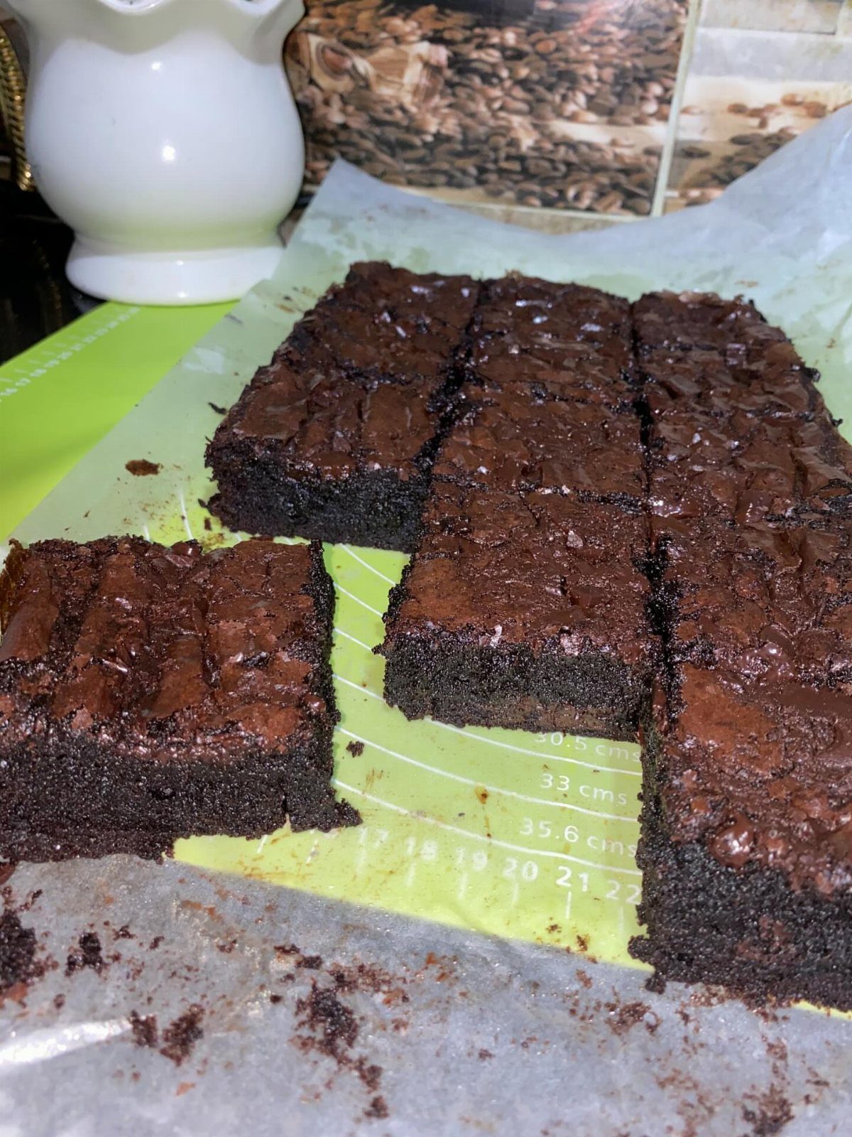 Chocolate brownies cut into squares on parchment paper and a green baking mat.