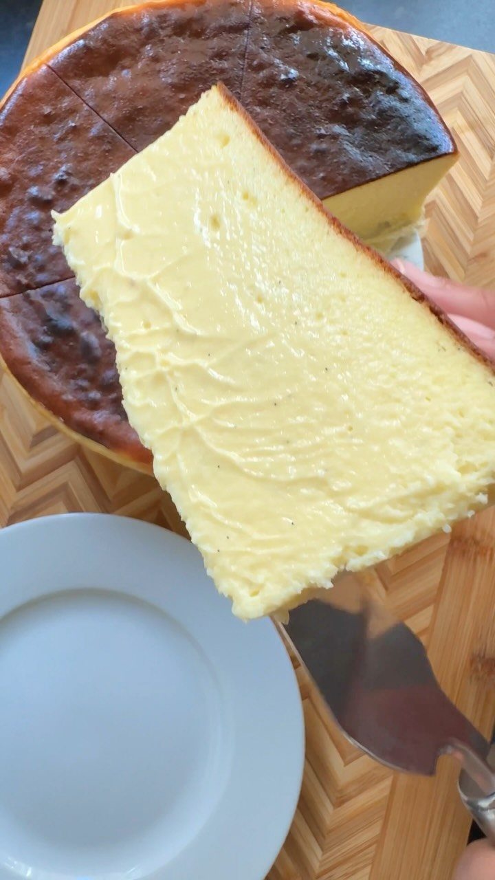 Slice of burnt basque cheesecake being lifted from a wooden cutting board.