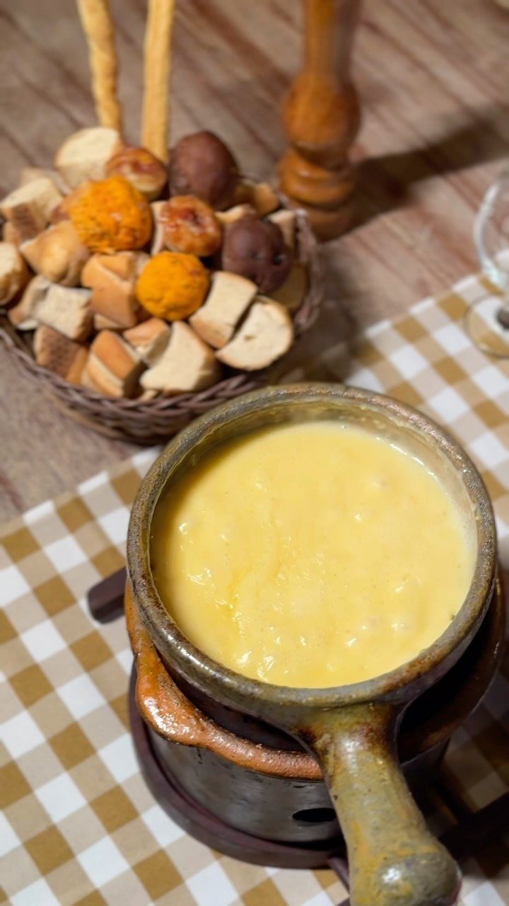 Cheese fondue in a ceramic pot with a basket of bread cubes.