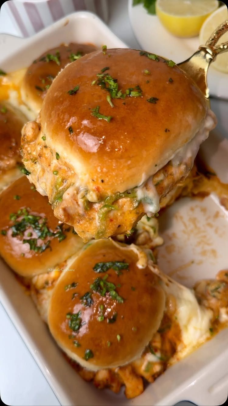 Sliders with glossy buns and melted cheese in a white baking dish.