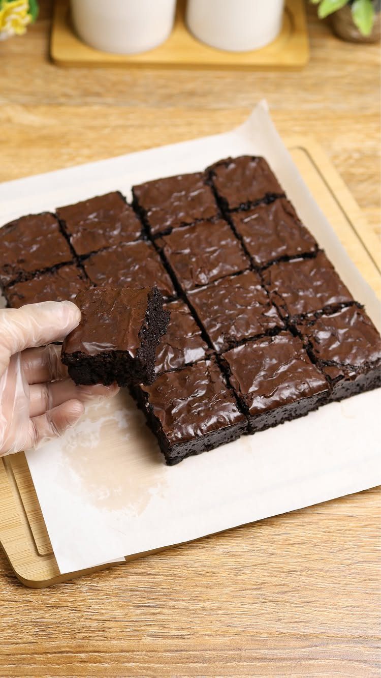 Chocolate brownies with glossy ganache topping on a wooden board with one piece lifted.