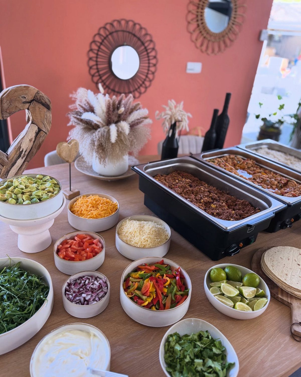 Taco bar spread with various toppings and meat in chafing dishes on wooden table