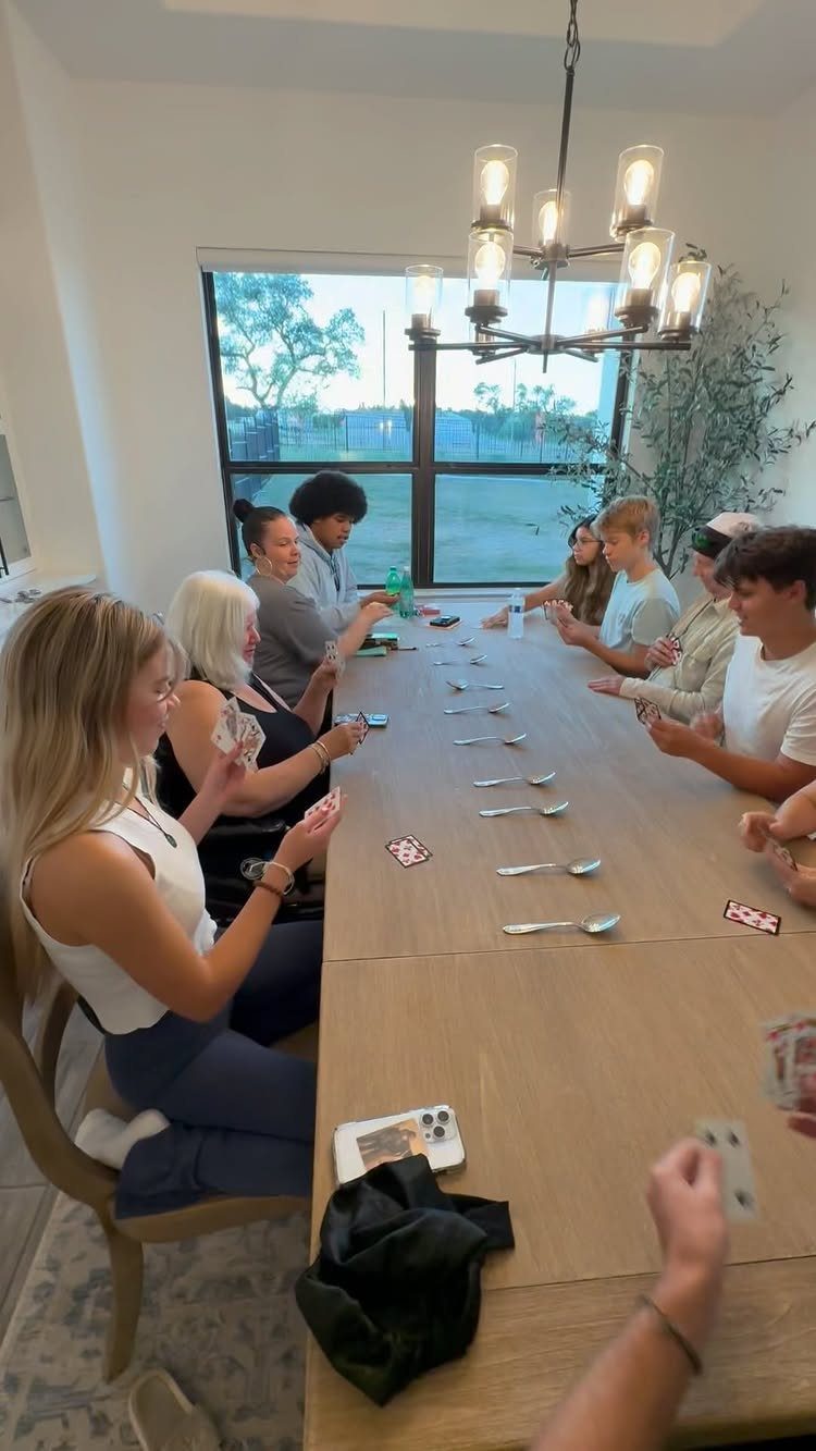 Young adults playing a card game with silver spoons on a wooden table.
