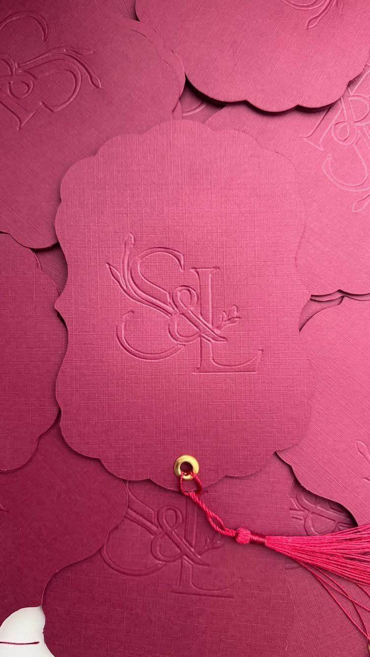 Magenta scalloped invitations with embossed monogram and a pink tassel detail.