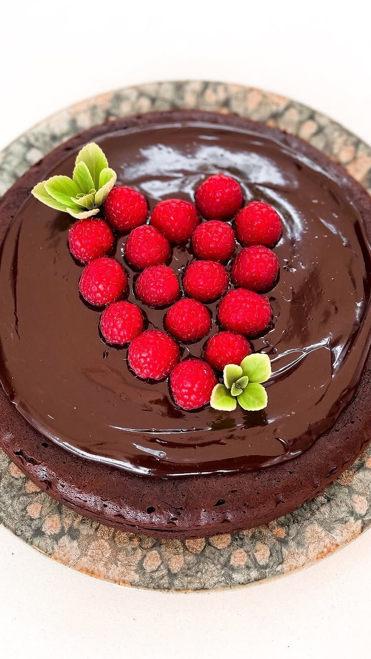 Chocolate cake with glossy ganache topped with raspberries in a heart shape.