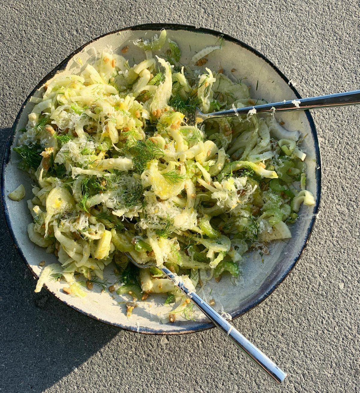 Fennel and celery salad with herbs and cheese in a ceramic bowl.