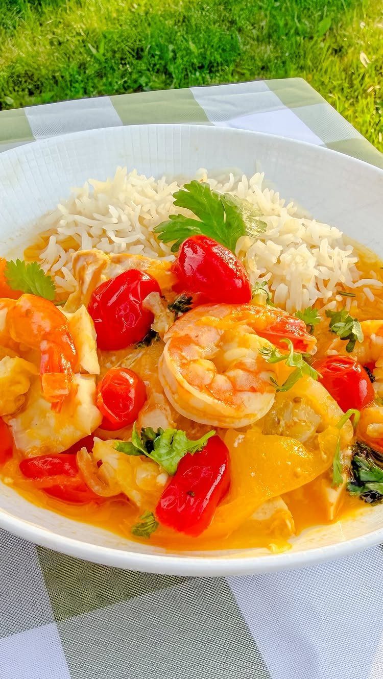 Fish and shrimp stew with red peppers and rice in a white bowl.