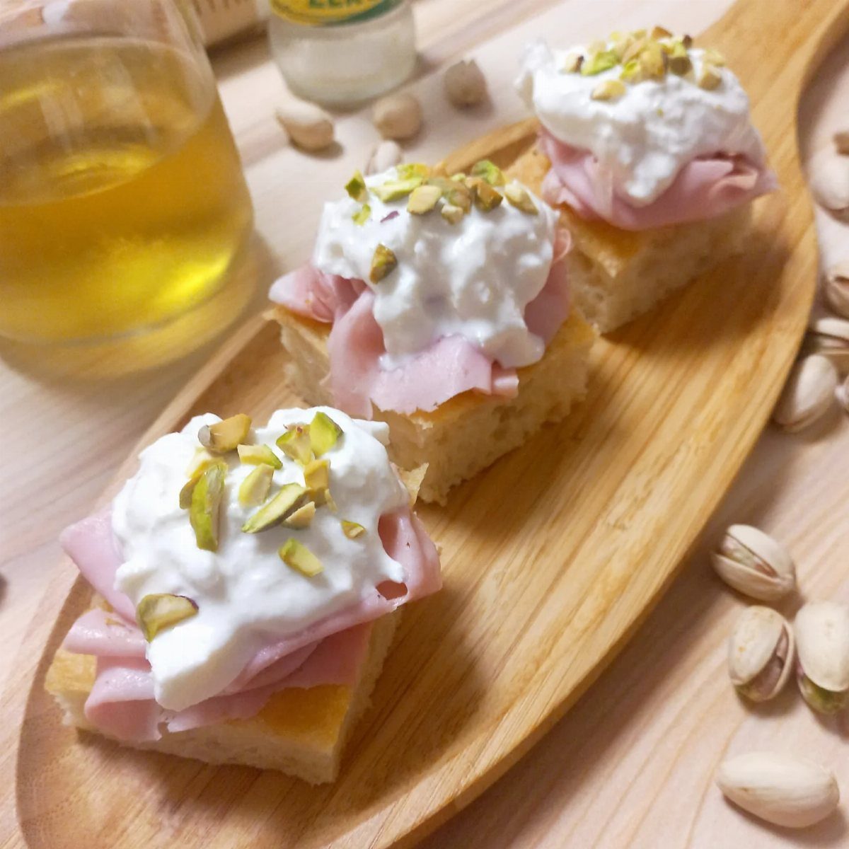 Three mortadella bites with white cream and pistachios on a wooden platter.