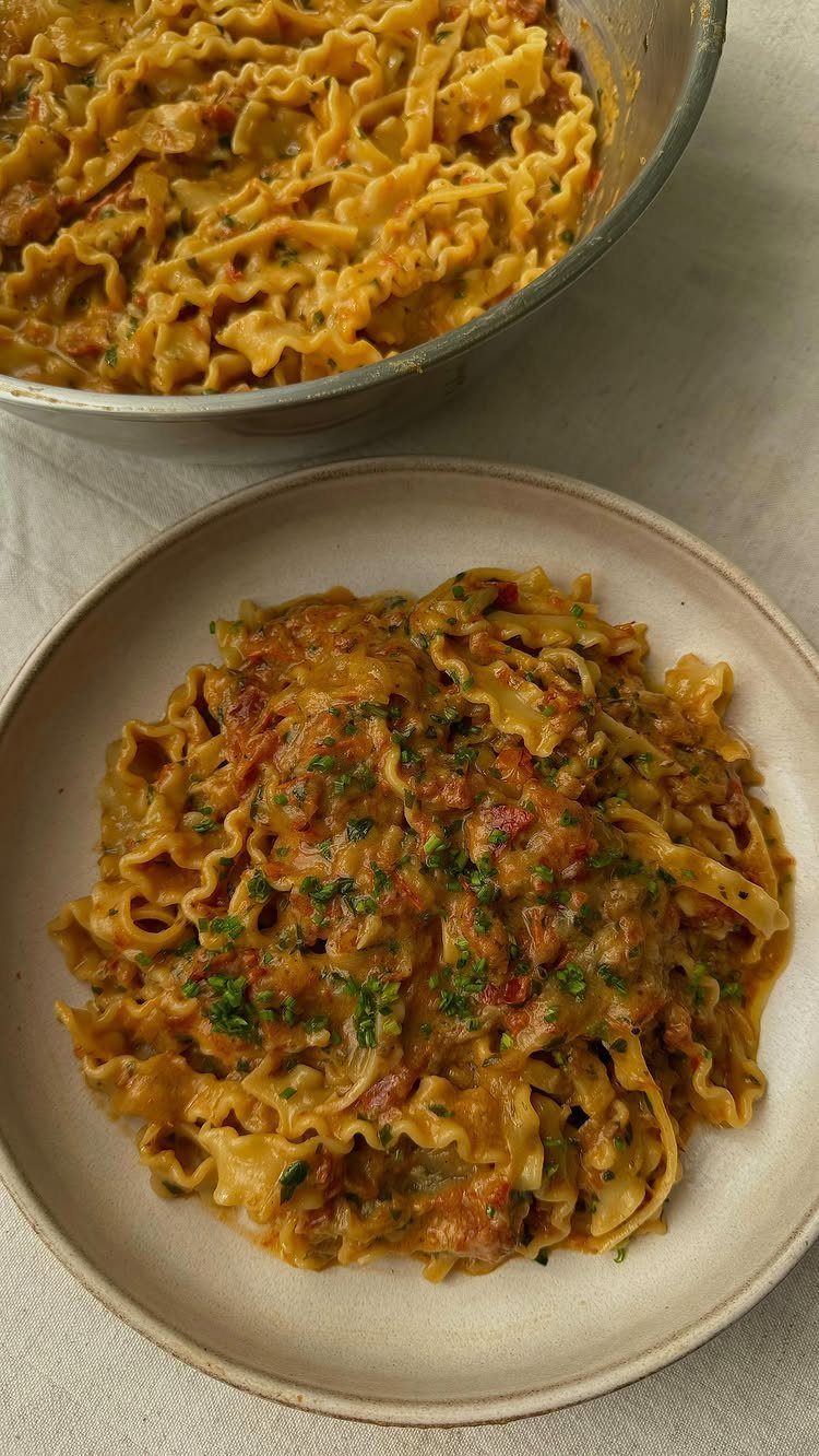 Ruffled pasta in a creamy brown sauce with herbs on a beige plate.