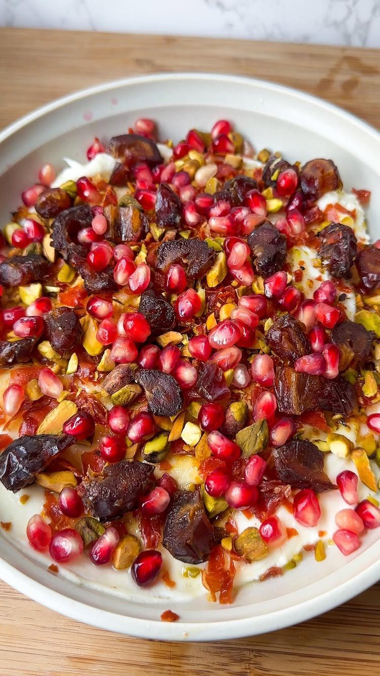 Creamy white dip topped with pomegranate seeds, dates, and pistachios in a bowl.