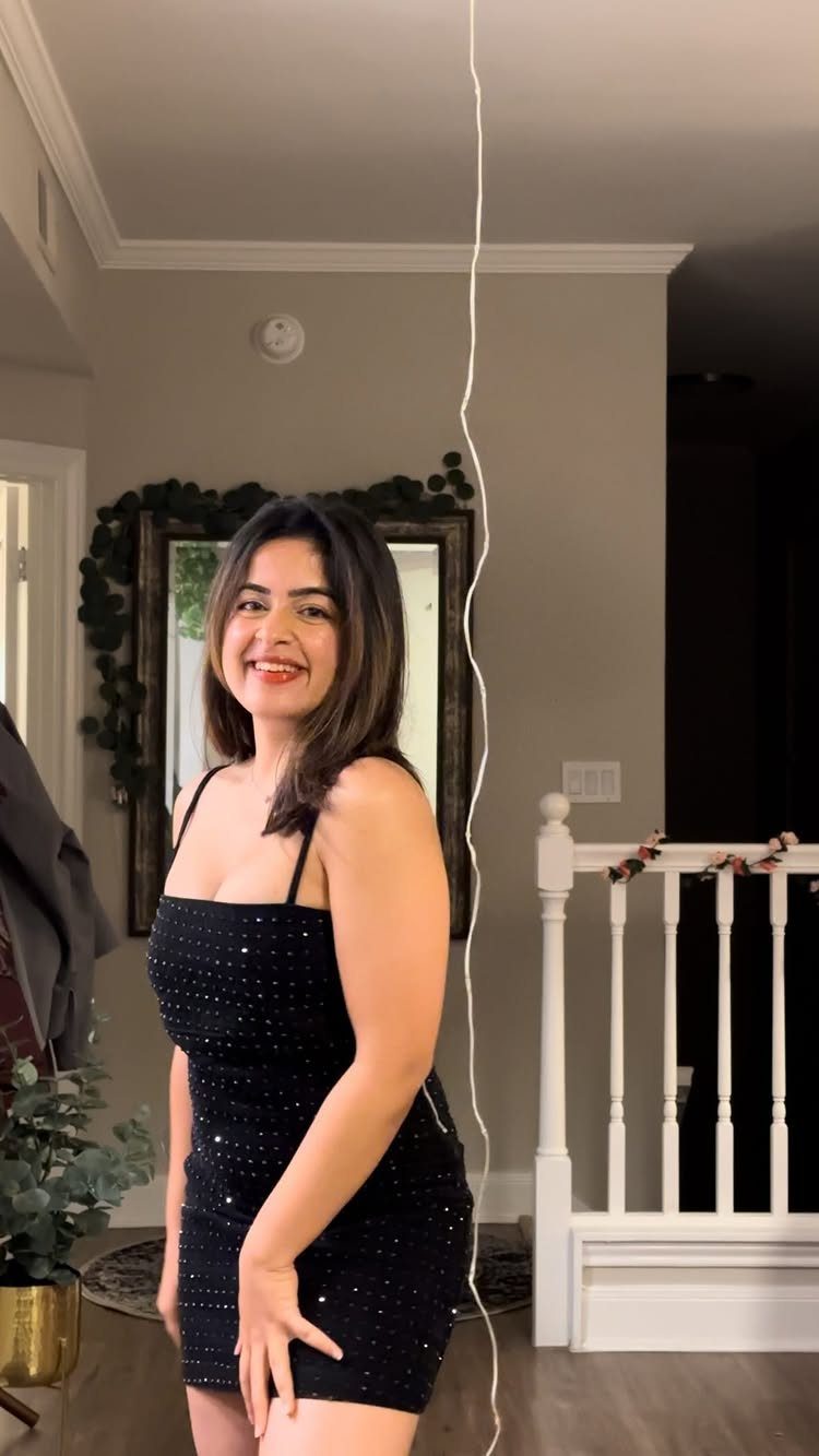 Woman smiling in a short black sequined dress standing in a home interior.