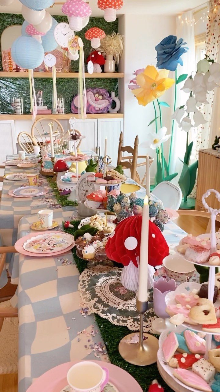 Whimsical dinner table with red mushrooms, giant paper flowers, and colorful sweets.
