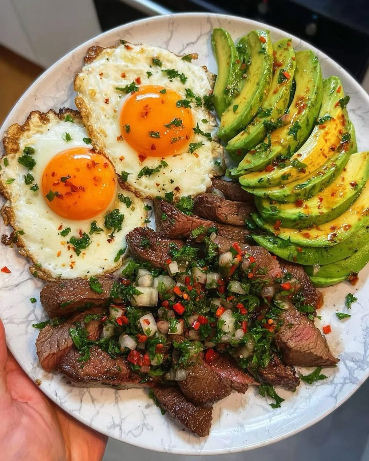 Plate of sunny-side-up eggs, sliced avocado, and steak with herb relish.