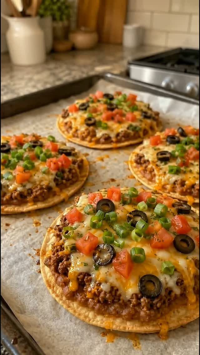 Four mini pizzas with various toppings on a baking sheet in a kitchen.