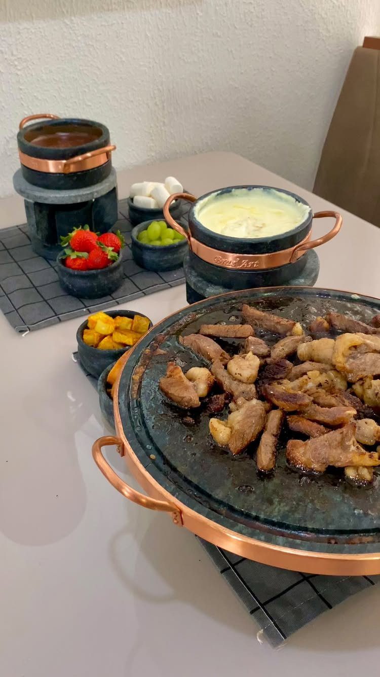 Fondue pots with cheese and chocolate alongside a meat griddle and fresh fruit.