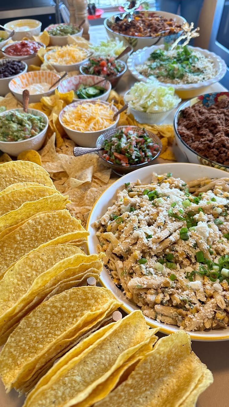 Taco bar spread with hard shells, guacamole, salsa, and seasoned meat bowls.