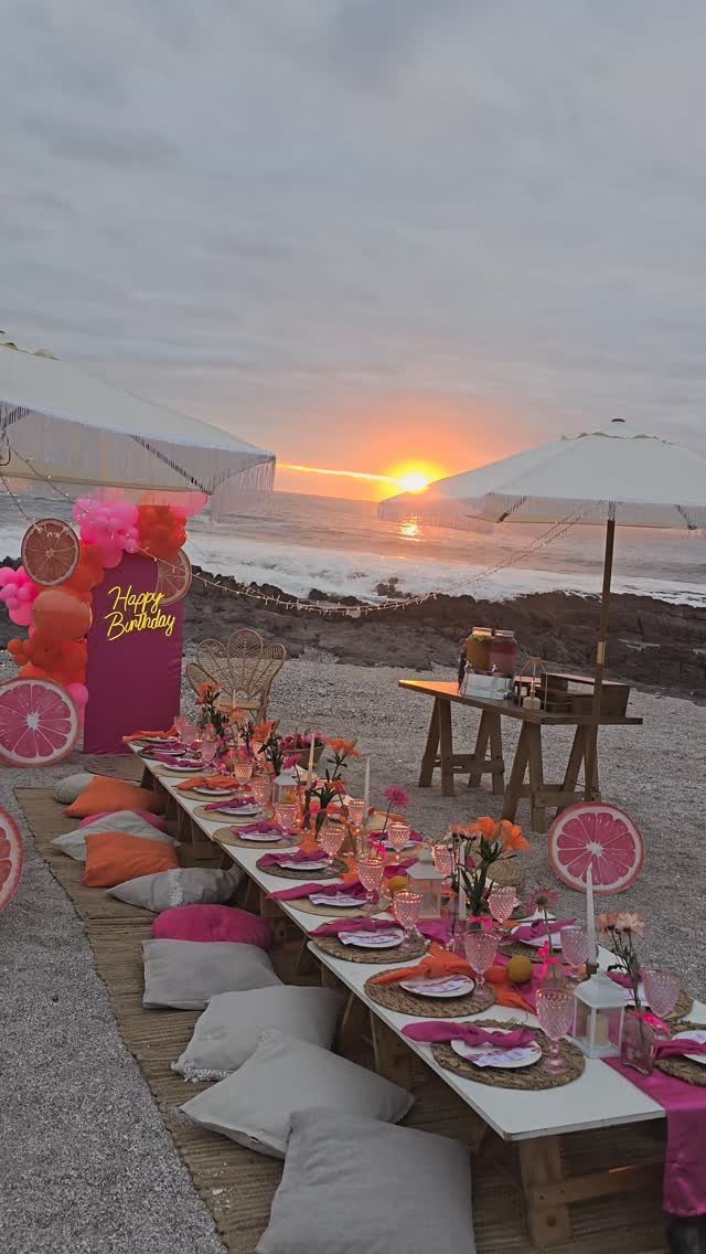 Low wooden table set with pink decor on a beach during a sunset.