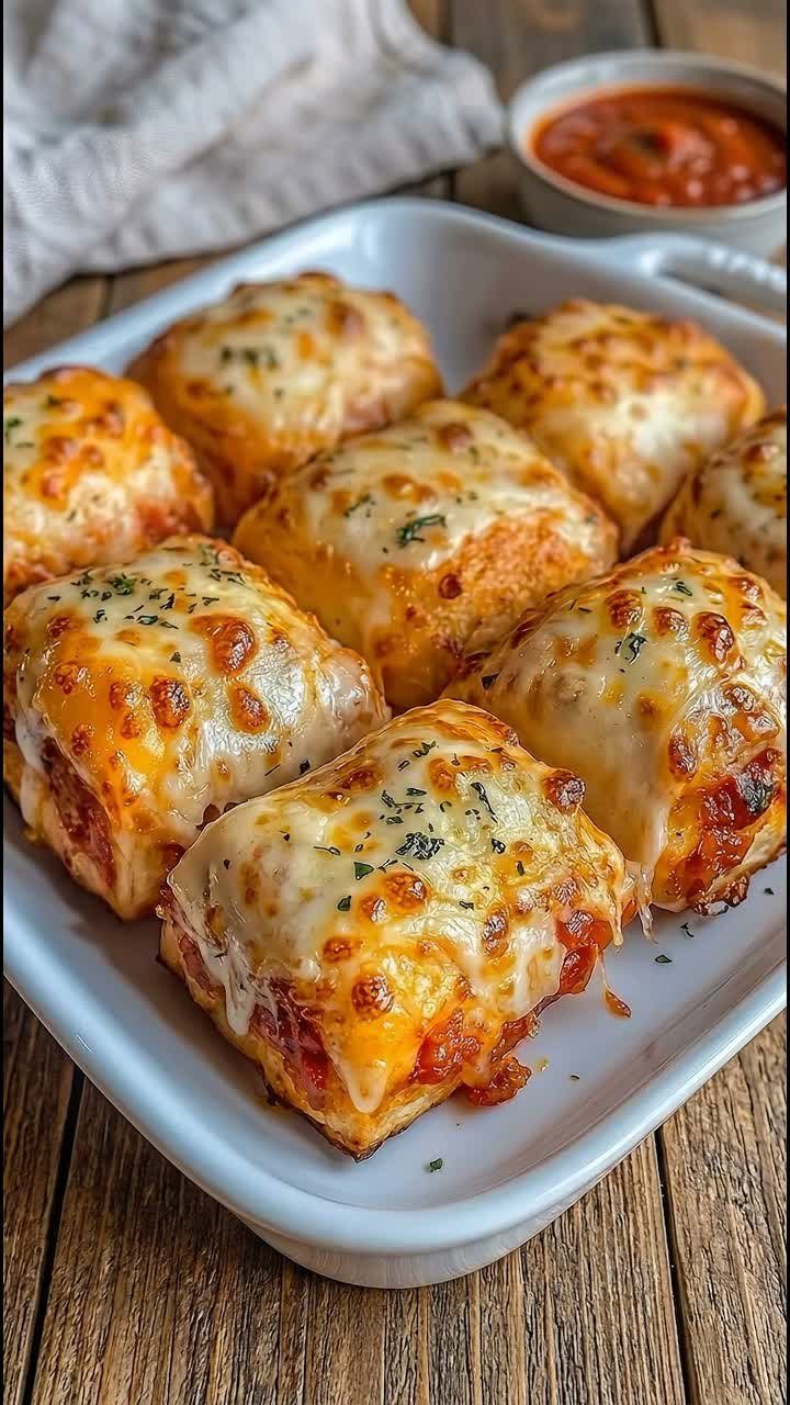 Baked cheesy pasta rolls in a white dish with a side of tomato sauce.