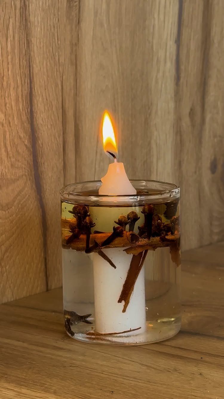 Lit floating candle in a glass jar with cinnamon sticks and cloves.