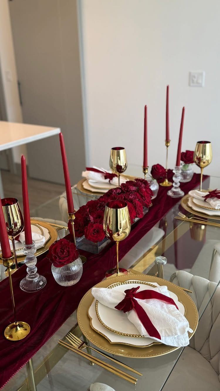 Elegant dinner table arrangement with burgundy runner, red roses, and gold tableware.