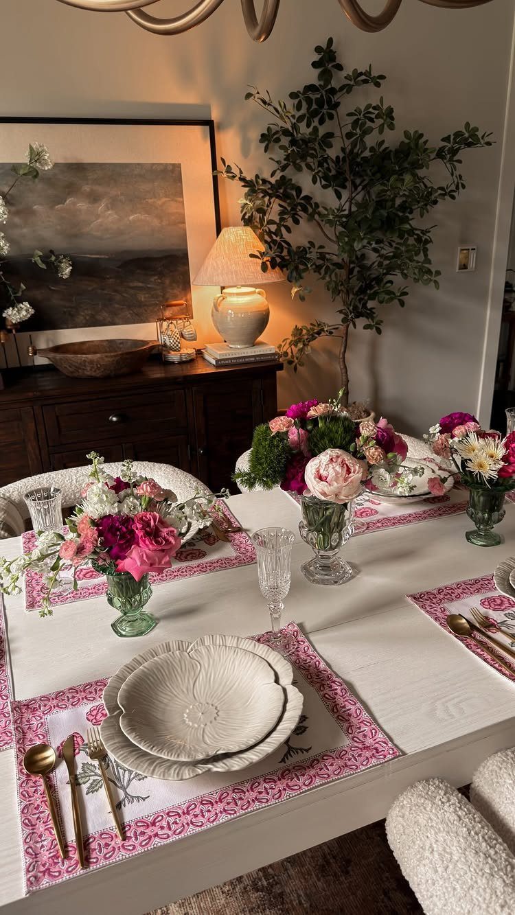 Fresh pink and white flowers in glass vases on a set dining table.